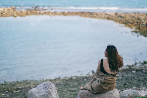 Preview: A beautiful asian woman enjoy sitting on the rock by the seashore