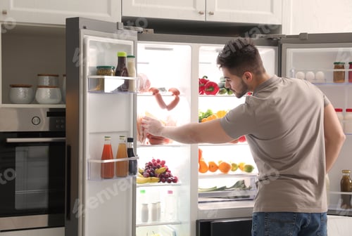 Preview: Young man taking ham out of refrigerator indoors, closeup