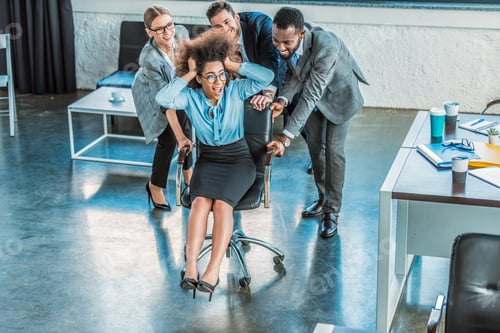 Preview: multicultural businesspeople having fun and racing colleague on chair in office