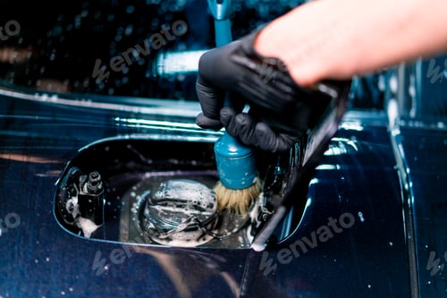 Preview: Close-up of a car wash employee washing the fuel cap space of a luxury blue car using a brush
