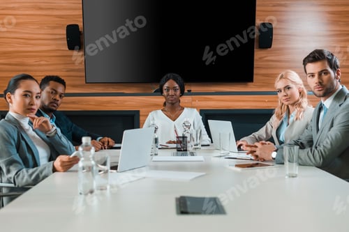 Preview: young, confident multicultural businesspeople sitting in conference hall with lcd screen on wall