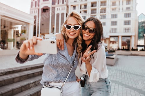 Preview: Well-dressed blonde lady making selfie with sister. Outdoor shot of romantic girls having fun in su