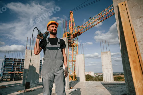 Preview: Standing and holding drill. Man in uniform is working on the construction site