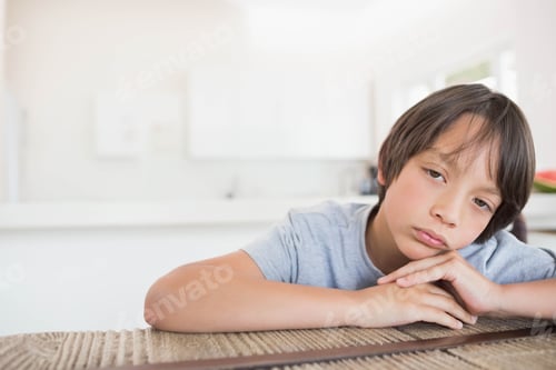 Preview: Boy leaning on woven tabletop in home kitchen with white cabinets and countertop, copy space