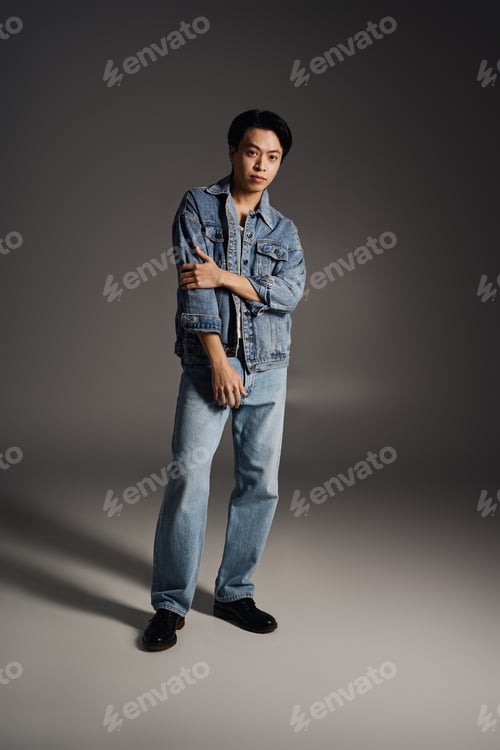 Preview: Young asian man showcases stylish denim look in a casual grey studio setting
