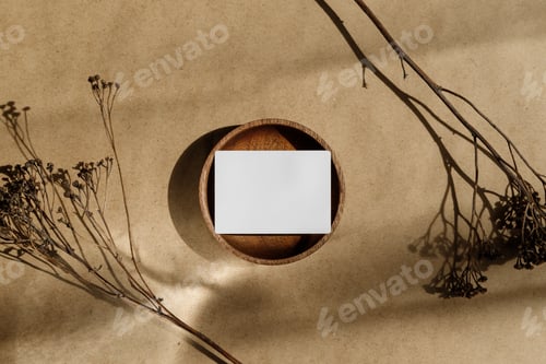 Preview: Top view of blank paper sheet card on wooden bowl with dry grass. Beige or sand tones.