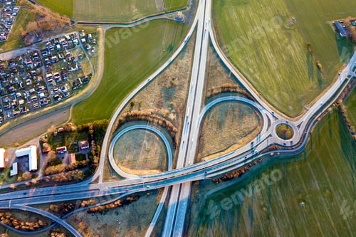 Preview: Aerial top view of modern highway road intersection, house roofs on spring green field