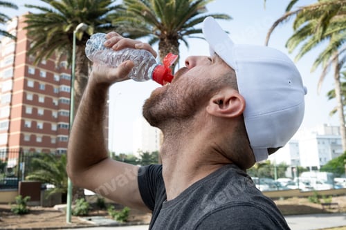 Preview: Young man drinking water after an outdoor workout in the city.