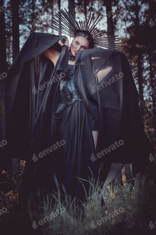 Preview: brunette woman in witch costume and crown on head holding hands with black textile near face,