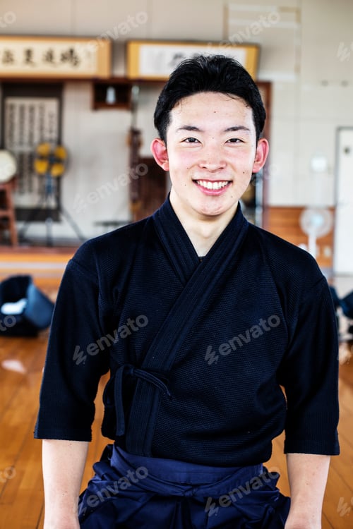 Preview: Male Japanese Kendo fighter standing in a gym, smiling at camera.