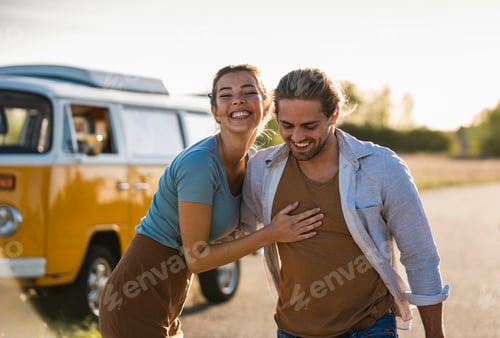 Preview: Happy couple doing a road trip with a camper, embracing on the road