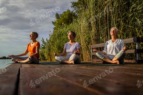 Preview: Group of senior woman doing yoga exercises by the lake.