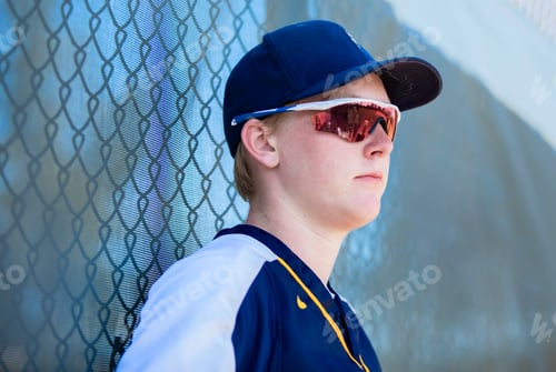 Preview: High school baseball player leaning against the fence wearing cap and sunglasses