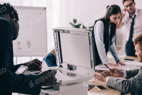 Preview: african american manager using copier in conference hall with colleagues blurred on background