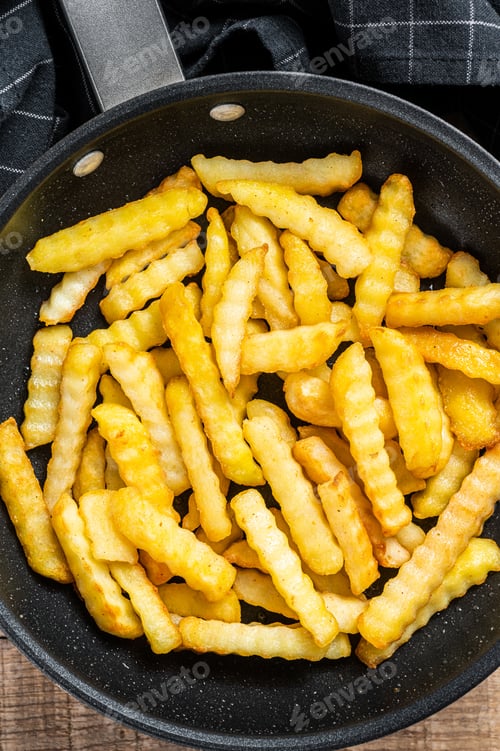 Preview: Fried Crinkle oven French fries potatoes sticks in a pan. Wooden background. Top view