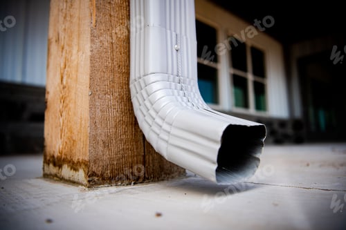 Preview: Closeup of a silver square labor hanging on a wooden pole with a house on a background