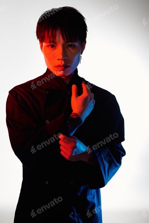 Preview: Stylish asian man poses confidently with a captivating expression in a vibrant light setting