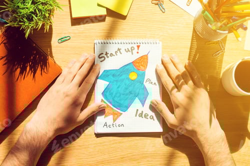 Preview: Start up. Close-up top view of man holding hands on paper with sketch laying on the wooden desk
