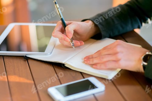 Preview: Writing notes and ideas on a notebook at a modern workspace with a tablet and smartphone nearby