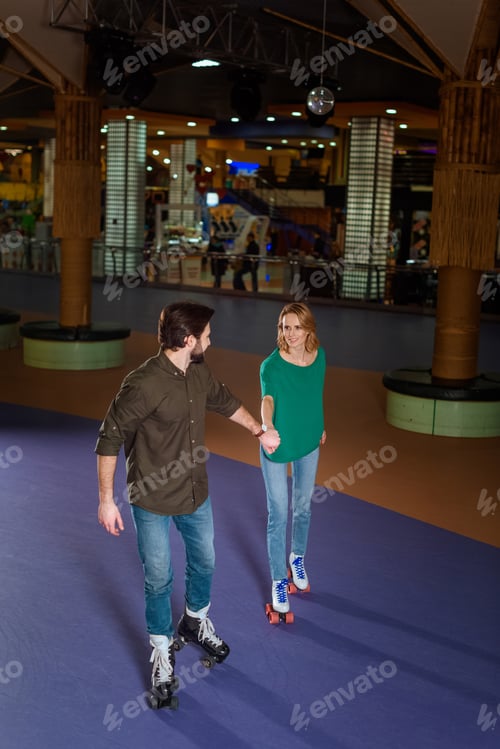 Preview: young couple holding hands while skating together on roller rink