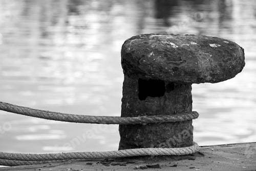 Preview: Grayscale shot of a rope curled over an old rusty metal pier