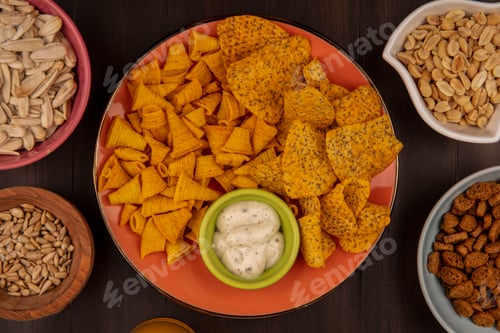 Preview: top view of tasty crispy chips on an orange dish with sauce on a bowl with white sunflower seeds on
