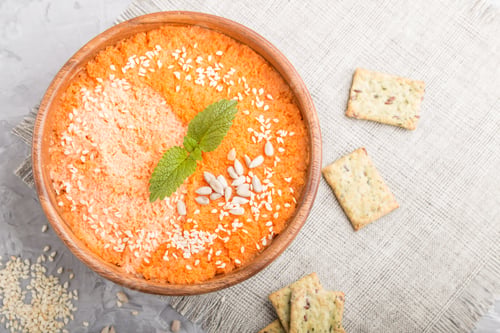 Preview: Carrot cream soup with sesame seeds and snacks in wooden bowl on a gray concrete background