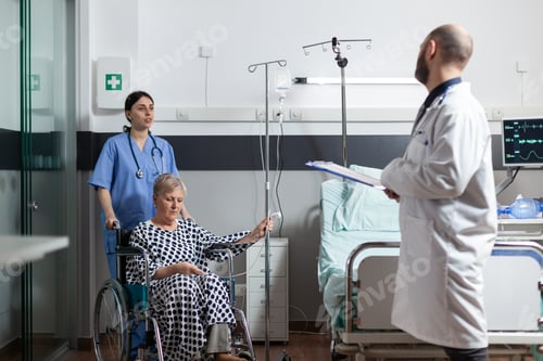 Preview: Sick senior woman sitting in wheel chair with iv drip bag attached on arm