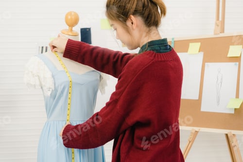 Preview: Asian female fashion designer working measuring dress on a mannequin clothing design at the studio.