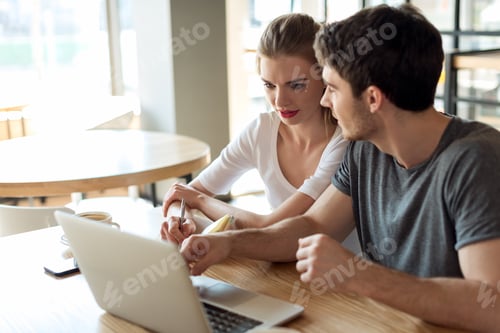 Preview: young couple working on laptop together while sitting at table in cafe