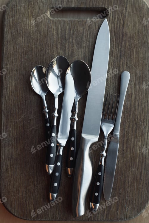 Preview: top view of arrangement of steel dinnerware on wooden cutting board