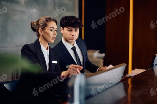 Preview: Two receptionists cooperating while working on a computer at hotel front desk.