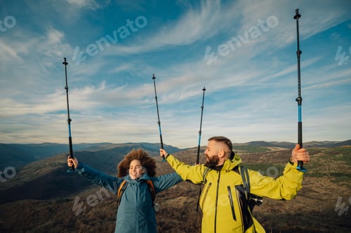 Preview: Hikers celebrating reaching mountain top with trekking poles
