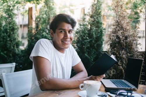 Preview: Cheerful Latin student e learning in street cafe