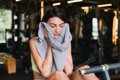 Preview: Fit caucasian beautiful woman in fitting sport wear at gym tired sweating clean face with towel
