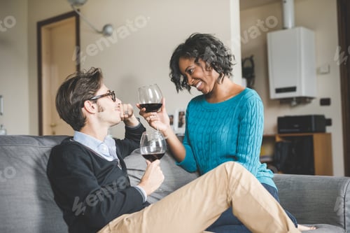 Preview: Multiethnic happy couple in love celebrating drinking wine indoor at home