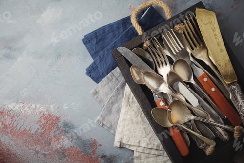 Preview: Vintage forks, spoons and knives in a dark old wooden box on a gray concrete or stone background. Se