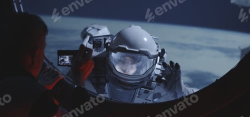 Preview: Medium Close-Up Of A Male Astronaut Filming His Spacewalking Crewmate From Inside A Spacecraft