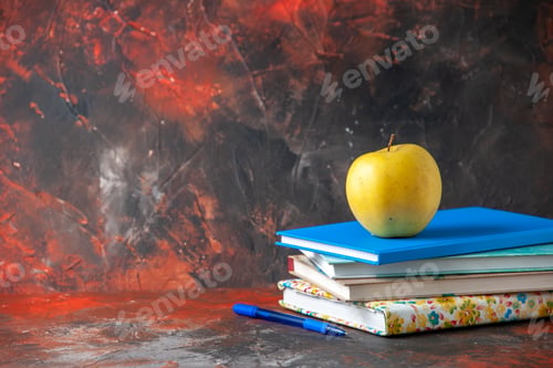 Preview: Horizontal view fresh yellow apple on stacked notebooks on the left side on dark background