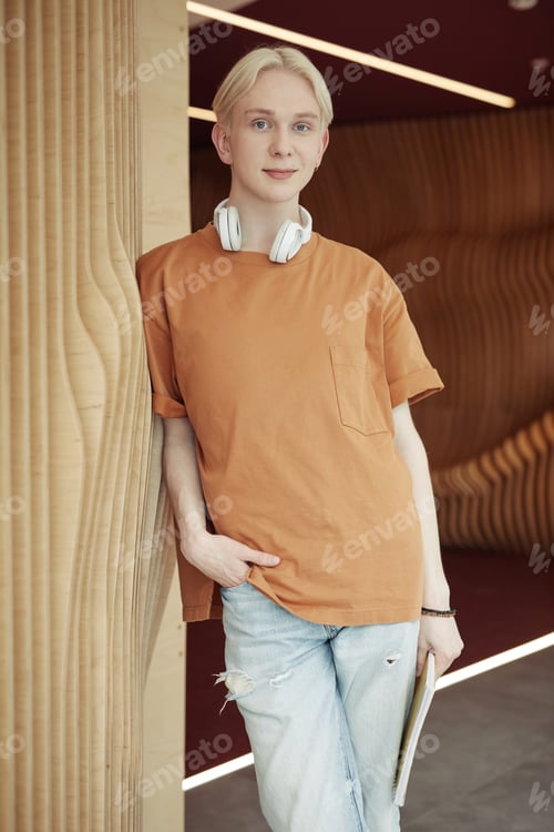 Preview: Smiling teenager in brown t-shirt and light blue jeans standing against wall
