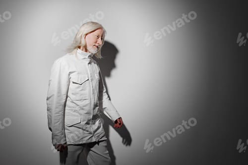 Preview: Fashionable elderly model in white clothing walking on a minimalist gray background, showcasing a