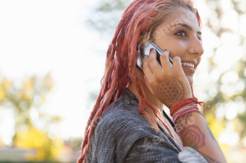 Preview: Young woman with pink dreadlocks chatting on smartphone in park