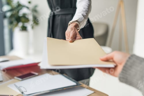 Preview: cropped shot of businesswoman giving envelope to colleague at workplace