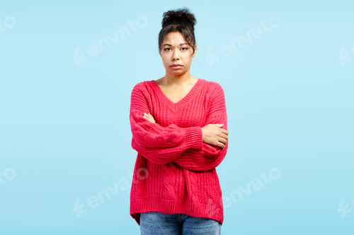 Preview: Serious young woman crossing arms showing confidence on blue background