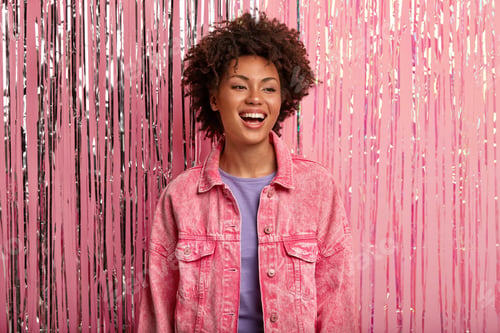 Preview: Young smiling African American female has minimal make up, wears pink jacket, laughs positively, bei