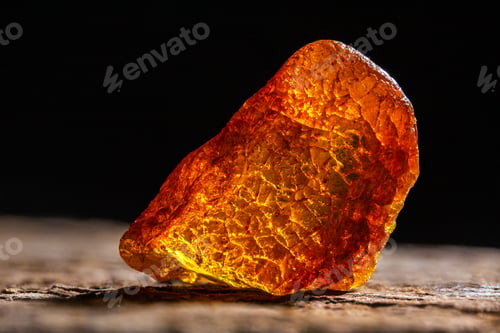 Preview: Natural amber. A piece of yellow transparent natural amber on large piece of dark stoned wood.