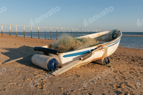 Preview: Aged fishing boat with nets on sandy seashore at sundown