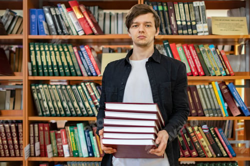 Preview: man in university holding stack of books (book shelf background) b