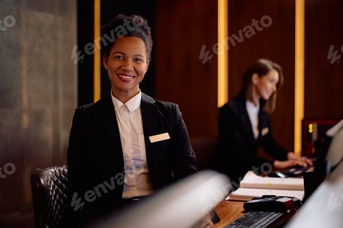 Preview: Happy black hotel manager at reception desk looking at camera.