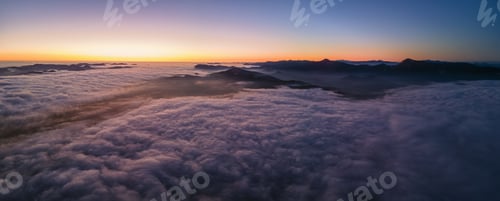 Preview: Aerial view of colorful sunrise over white dense fog with distant dark silhouettes of mountain